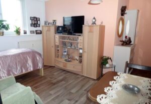 Innenansicht eines gemütlichen Wohnzimmers mit Fernseher, Schränken und Dekorationen.