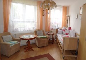 Gemütlicher Wohnraum mit zwei Sesseln, einem Tisch und einem Pflegebett.