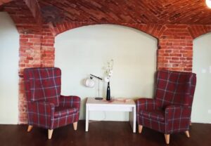 Ein gemütlicher Sitzbereich mit zwei karierten Sesseln und einem Tisch zwischen ihnen vor einer Wand aus roten Ziegelsteinen.
