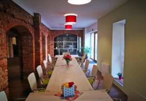 Ein modern eingerichteter Besprechungsraum mit einem langen Tisch und Stühlen, umgeben von Ziegelwänden.