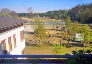 Ein zweistöckiges Gebäude mit Blick auf eine Landschaft mit Bäumen, einem Spielplatz und einem kleinen Teich.
