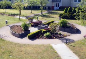 Ein gepflegter kleiner Gartenbereich mit Sitzbänken und blühenden Pflanzen in einem Wohngebiet.