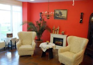 Gemütliche Sitzecke in einem Raum mit roten Wänden, zwei beigen Sesseln, einem kleinen Tisch, einem elektrischen Kamin und Dekorationen.