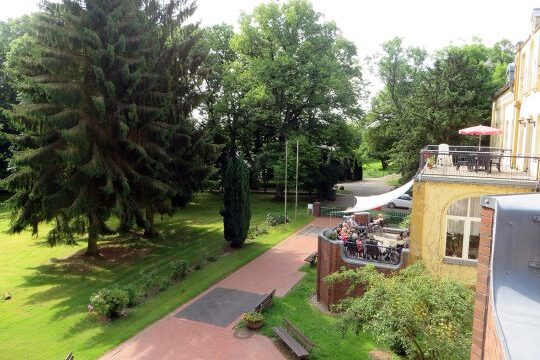 Blick auf eine Gartenanlage mit umgebenden Bäumen und einem Gebäude mit Terrasse.