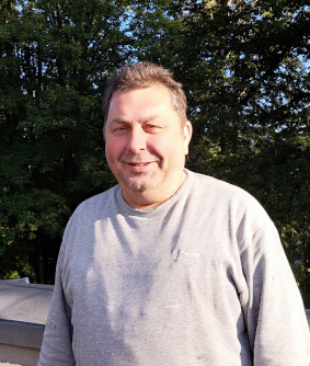 Ein Mann steht im Freien mit Bäumen im Hintergrund.