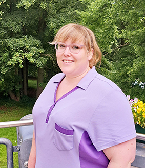 Eine Person steht auf einem Balkon vor einer grünen Baumkulisse.