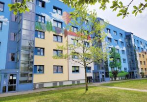 Außenansicht eines bunt bemalten mehrstöckigen Gebäudes mit Bäumen im Vordergrund.