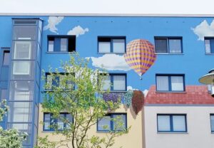 Ein Gebäude mit einer bemalten Fassade, die einen blauen Himmel, weiße Wolken und einen Heißluftballon zeigt.