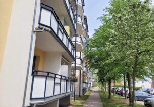 Ansicht eines Wohngebäudes mit Balkonen und Bäumen daneben.