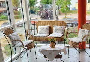 Gemütliche Sitzecke mit Korbmöbeln in einem Raum mit großen Fenstern.