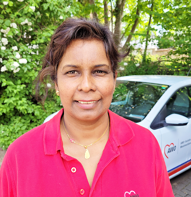 Eine Frau in rotem Poloshirt steht vor einem Auto mit AWO-Logo.