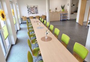 Innenansicht eines hellen Gemeinschaftsraums mit langen Tischreihen.
