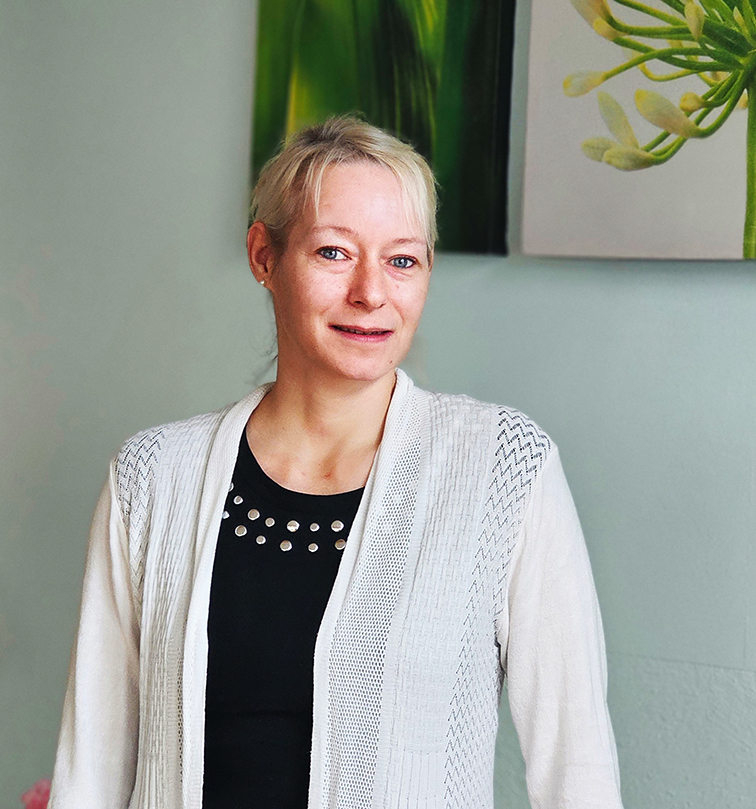 Eine Person steht vor einem hellen Hintergrund und lächelt leicht.