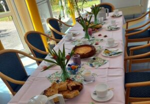 Eingedeckter Tisch mit frühlingshafter Dekoration und Kuchenauswahl.