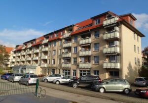 Mehrstöckiges Wohngebäude mit Balkonen und parkenden Autos davor