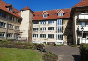 Mehrstöckiges Gebäude mit Rasenfläche und Bänken im Vordergrund