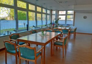 Innenansicht eines hellen, einladenden Gemeinschaftsraumes mit Tischen und Stühlen.