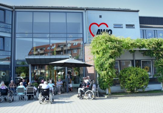 Außenansicht eines AWO-Gebäudes mit Menschen in Rollstühlen und am Tisch sitzend