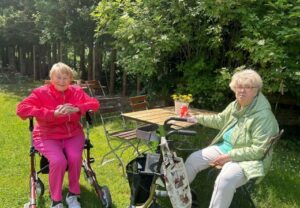 Zwei ältere Frauen sitzen im Garten an einem Tisch