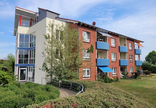 Außenansicht eines mehrstöckigen Gebäudes mit roter Klinkerfassade und blauen Balkonen.