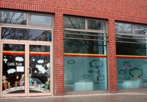 Eingang des Café FuN mit Schaufenstern, die Wolkenmotive zeigen.