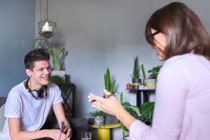Jugendlicher sitzt auf einem Sofa und unterhält sich mit einer Frau, die ihm gegenüber sitzt.