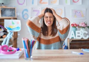 Frau in einem Klassenzimmer, hält sich frustriert den Kopf.