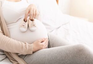 Schwangere Frau hält Babyschuhe auf ihrem Bauch
