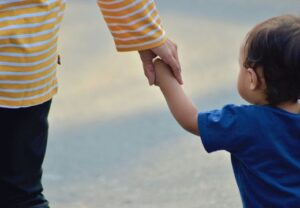 Nahaufnahme eines Kleinkindes, das die Hand einer erwachsenen Person hält.