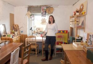 Eine Person steht in einem kreativ eingerichteten Raum mit Bastelmaterialien.