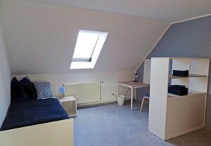 Einrichtung eines hellen Zimmers mit Schreibtisch und Bett unter Dachschräge