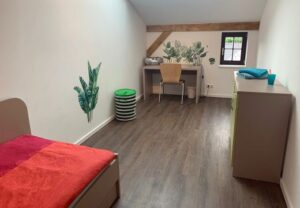 Ein einfach eingerichtetes Zimmer mit Bett, Schreibtisch und Kommode.