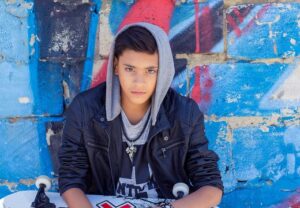 Jugendlicher mit Kapuzenpullover und Skateboard vor einer Graffiti-Wand