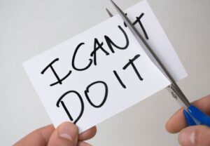 Eine Karte mit der Aufschrift 'I CAN'T DO IT' wird mit einer Schere so zerschnitten, dass 'CAN'T' durchtrennt wird.