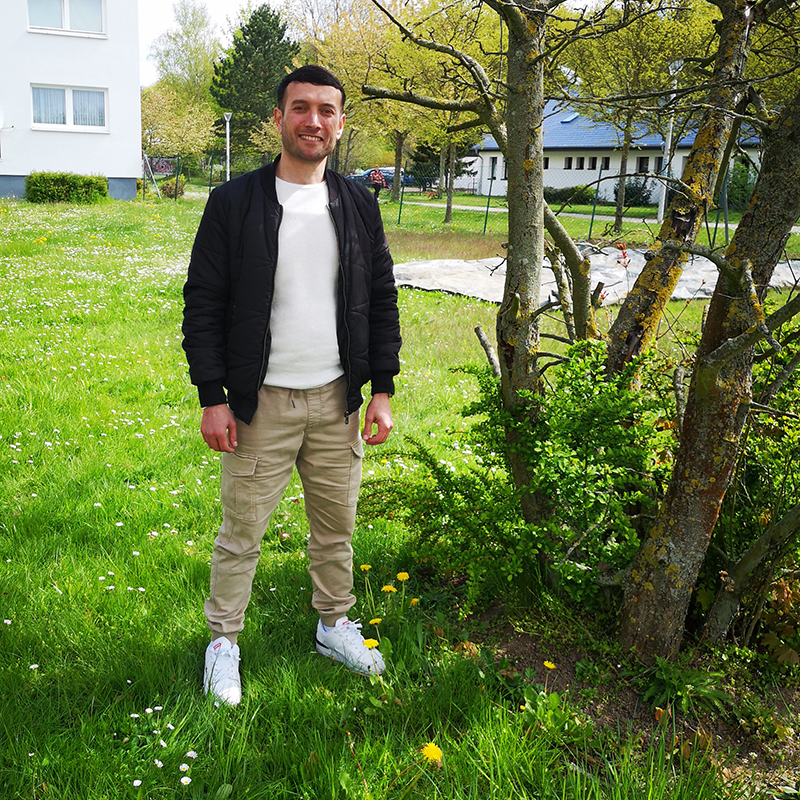Mann steht auf einer Wiese neben einem Baum