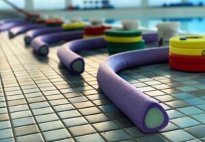 Schwimmnudeln und Schwimmbretter am Beckenrand eines Schwimmbads