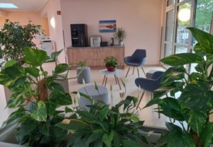 Innenansicht eines modernen Wartezimmers mit grünen Pflanzen, Sitzmöbeln und einem Kaffeeautomaten