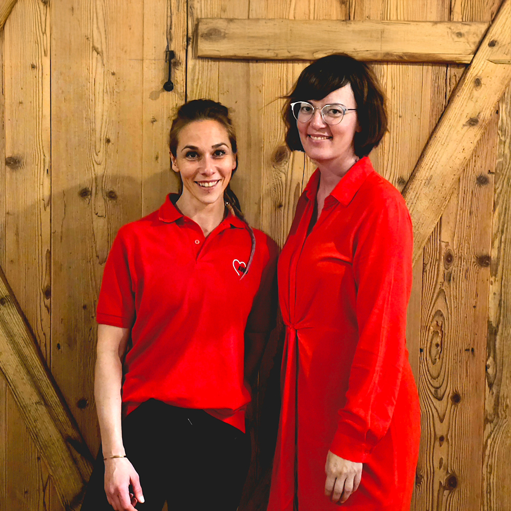 Zwei Frauen in roten Oberteilen vor Holzwand