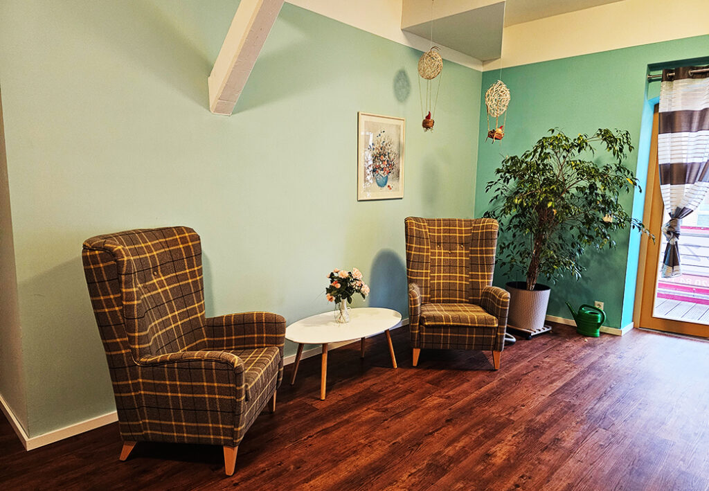 Ein gemütlich eingerichteter Raum mit zwei karierten Sesseln und einem kleinen Tisch mit Blumen darauf.