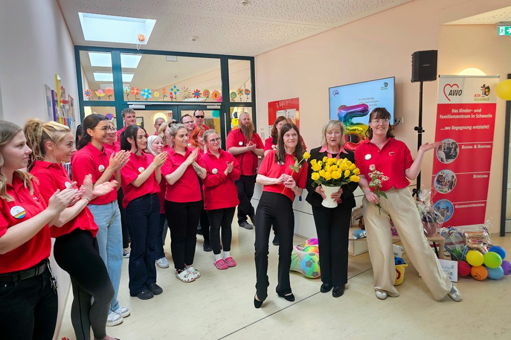 Eine Gruppe von Menschen in roten Polohemden steht in einem Raum und applaudiert.