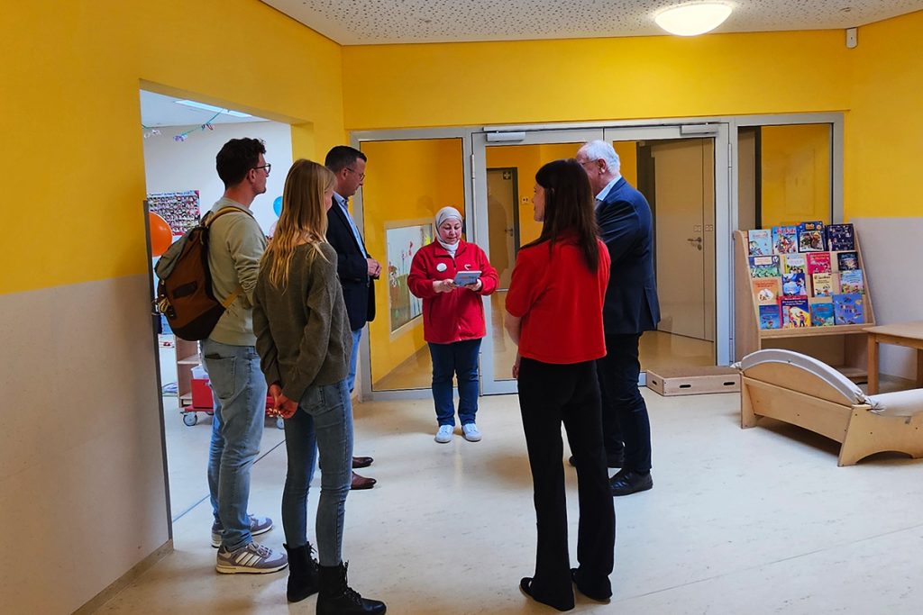 Eine Gruppe von Menschen steht in einem hellen Raum mit gelben W&auml;nden.