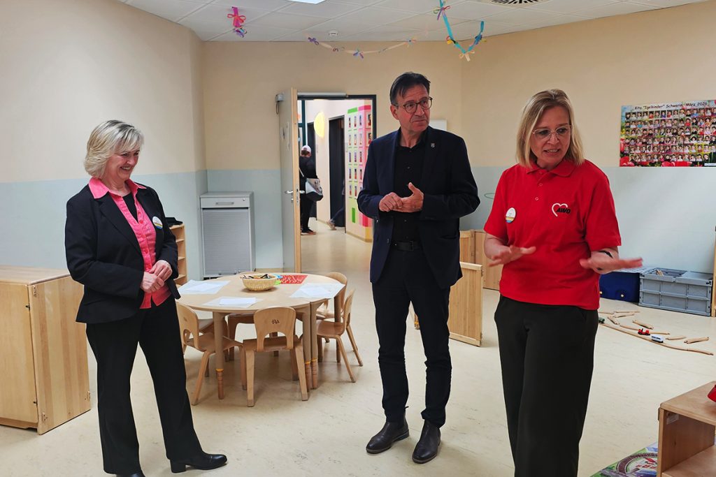 Drei Personen stehen in einem Raum miteinander redend, links und rechts jeweils eine Frau und in der Mitte ein Mann.