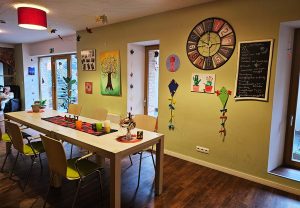 Innenansicht eines farbenfroh dekorierten Raumes mit einem langen Tisch und Stühlen.