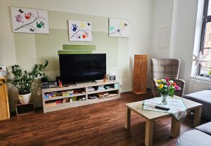 Gemütlicher Wohnbereich mit Fernseher, Sessel und Blumenstrauß auf dem Tisch