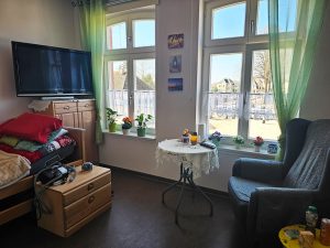 Ein Wohnzimmer in einem Pflegeheim mit einem Sessel, Fenster und Fernseher.
