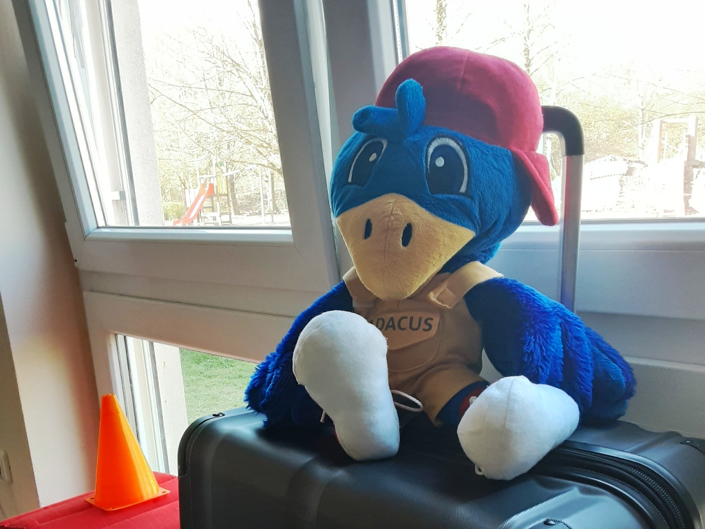 Ein Plüschtier eines Vogels mit rotem Basecap sitzt auf einem Koffer.