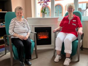Zwei Frauen sitzen in Stühlen vor einem Kamin.