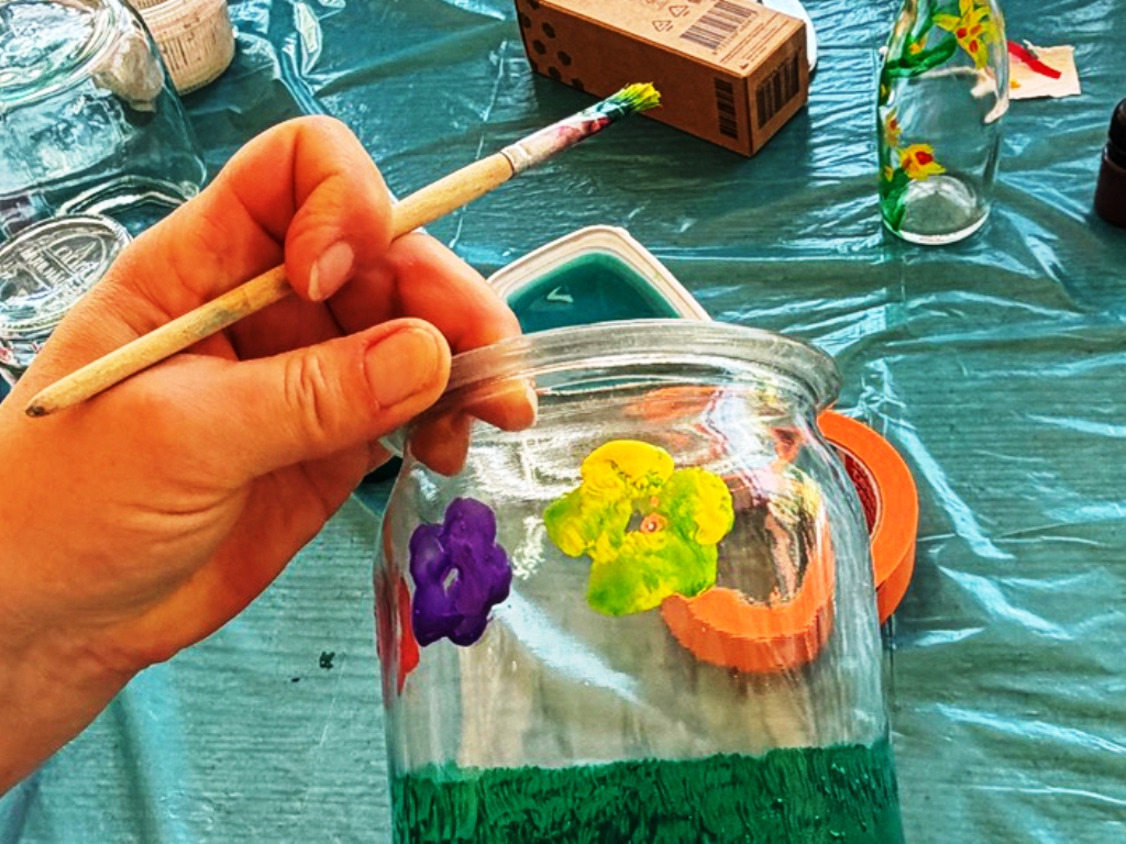 Eine Hand hält einen Pinsel, mit dem ein Glas bemalt wird.