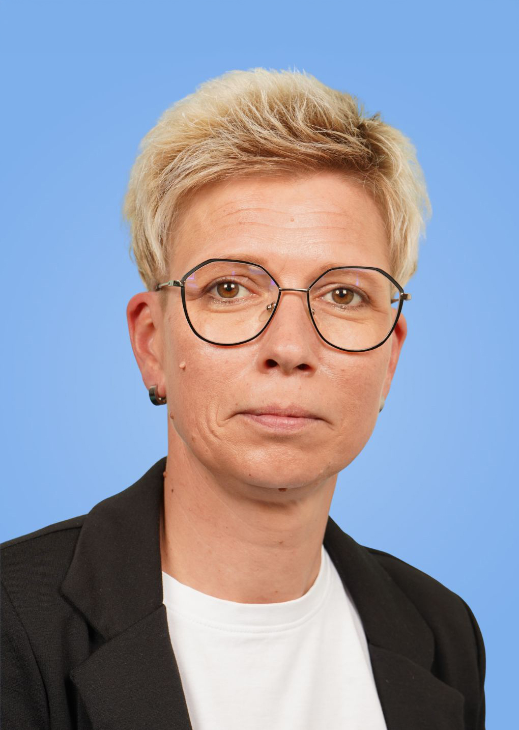 Porträtaufnahme einer Person mit kurzen, blonden Haaren und Brille vor einem blauen Hintergrund.
