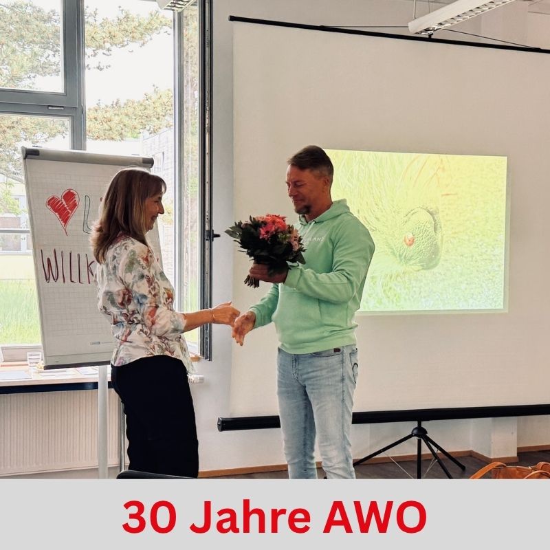 Eine Frau und ein Mann stehen in einem Raum. Der Mann überreicht der Frau einen Blumenstrauß.